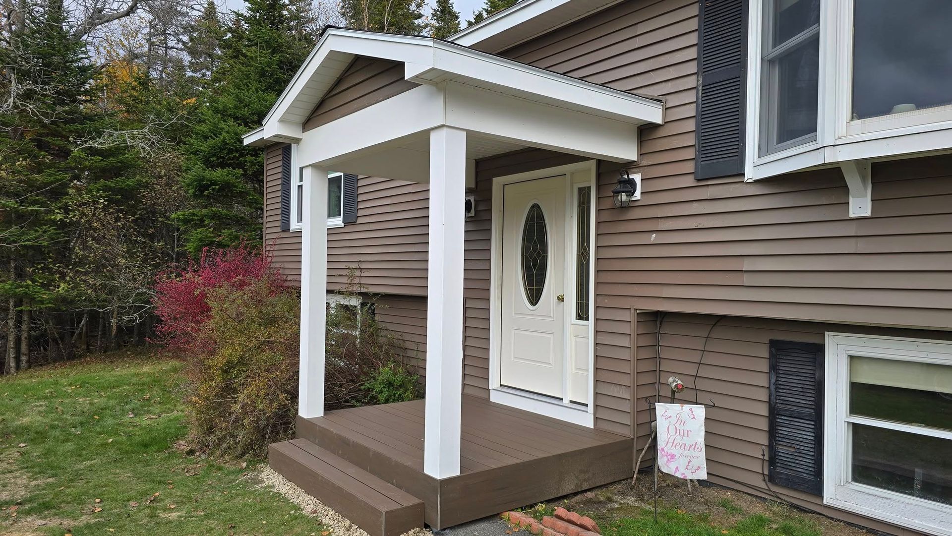 Front porch entrance with white door, tan siding, brown posts, and a small roof overhang