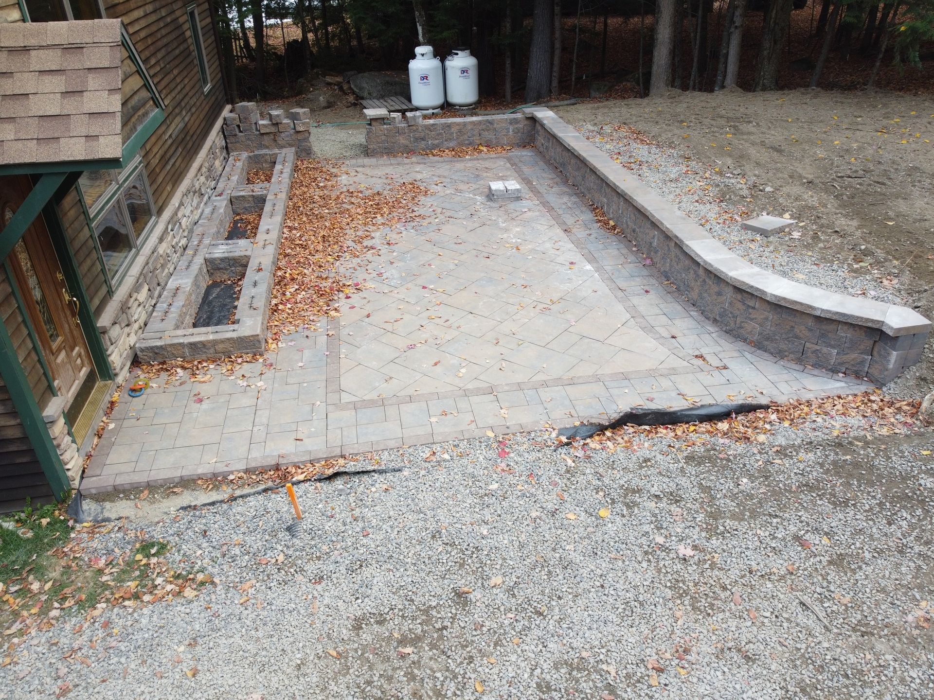 Empty concrete patio with scattered leaves, low curved retaining wall, and two white tanks near a fence.