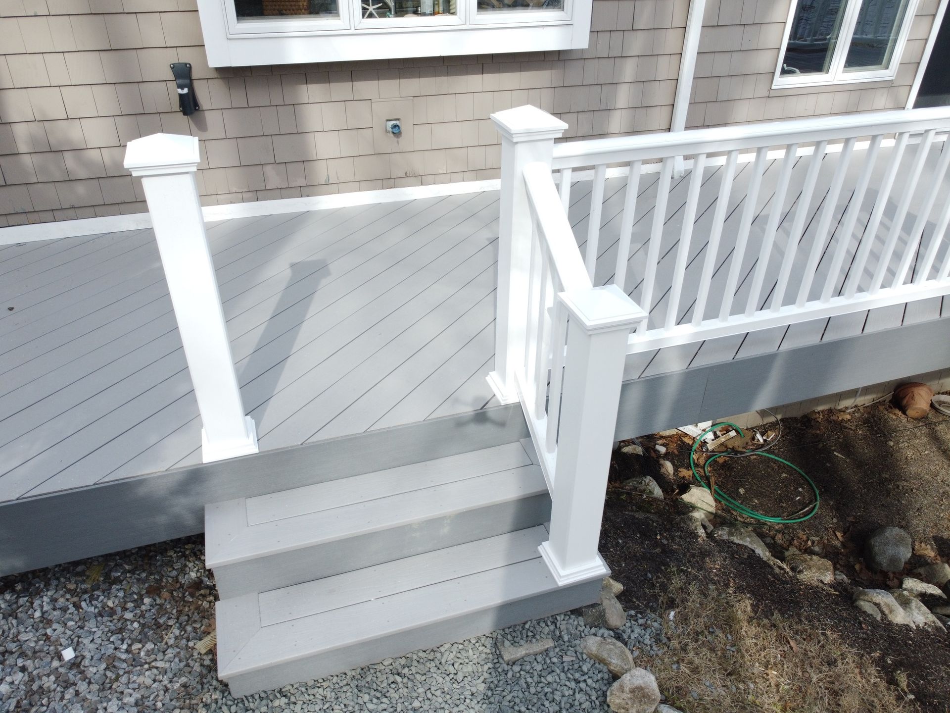Front porch steps with white railings leading to a gray deck beside a house