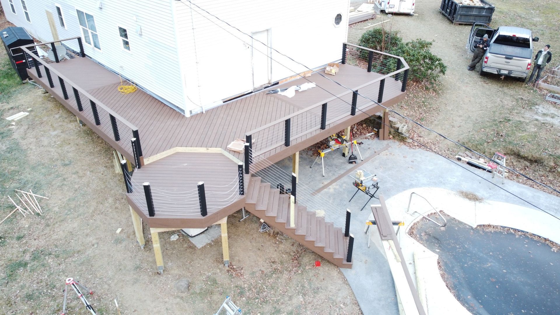 Aerial view of a house deck with stairs, a ramp, and a driveway beside parked vehicles.