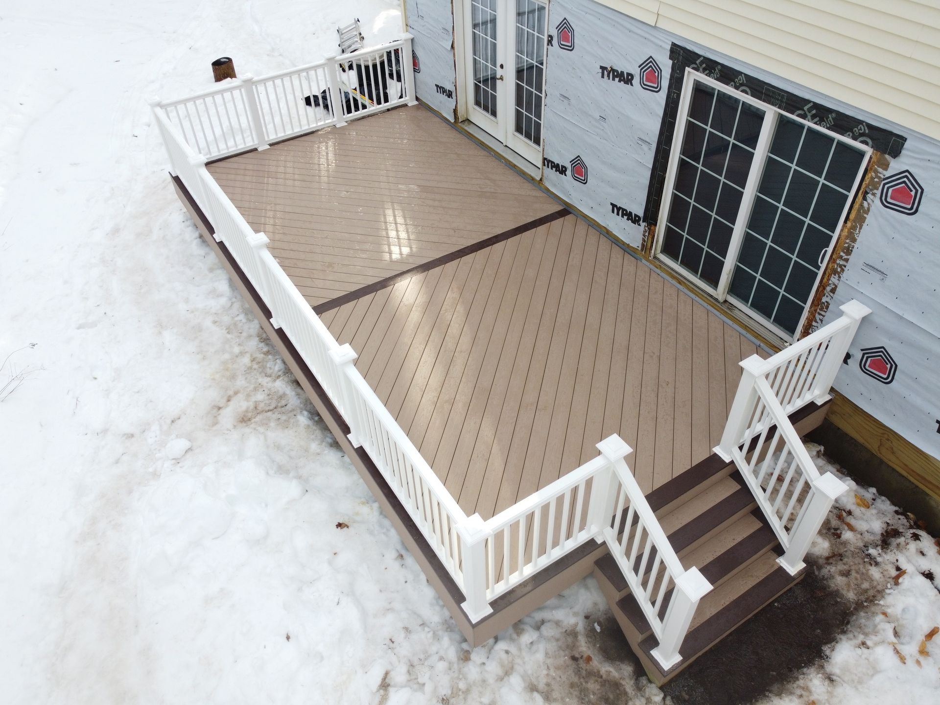 Small rooftop deck with white railings, tan floorboards, and stairs beside house siding and windows