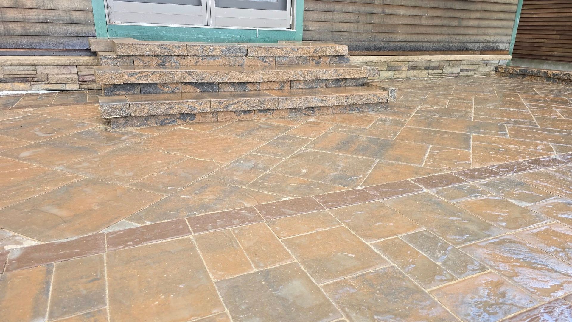 Stone patio leading to a wooden door, with worn steps and a muddy, patterned surface.