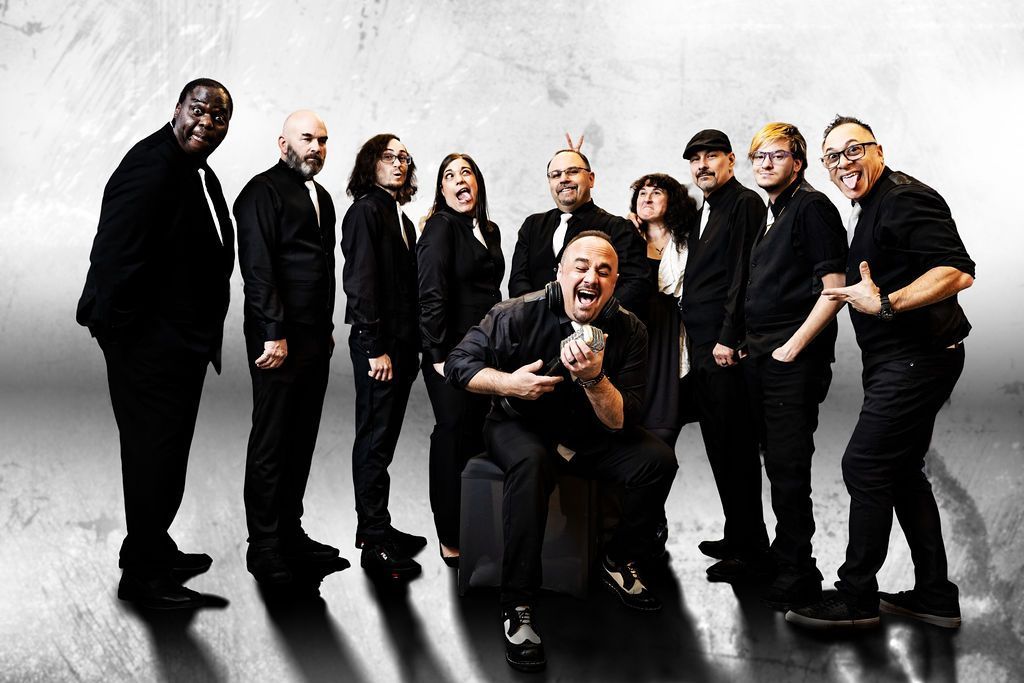 Band of ten people, all in black outfits, posing for a photo under blue lights.