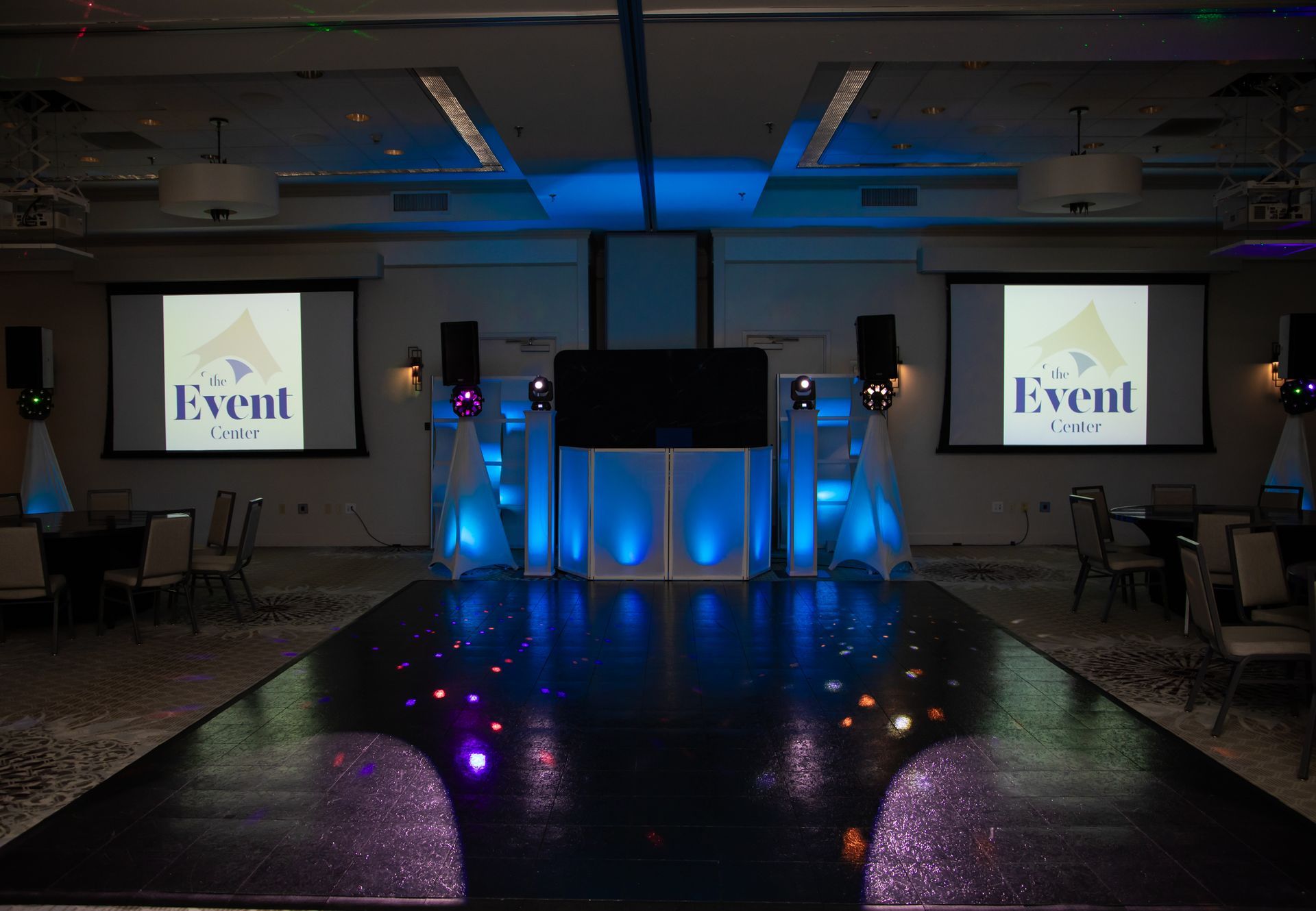 A runway lit with blue lights and a stage setup for an event, with screens and speakers.