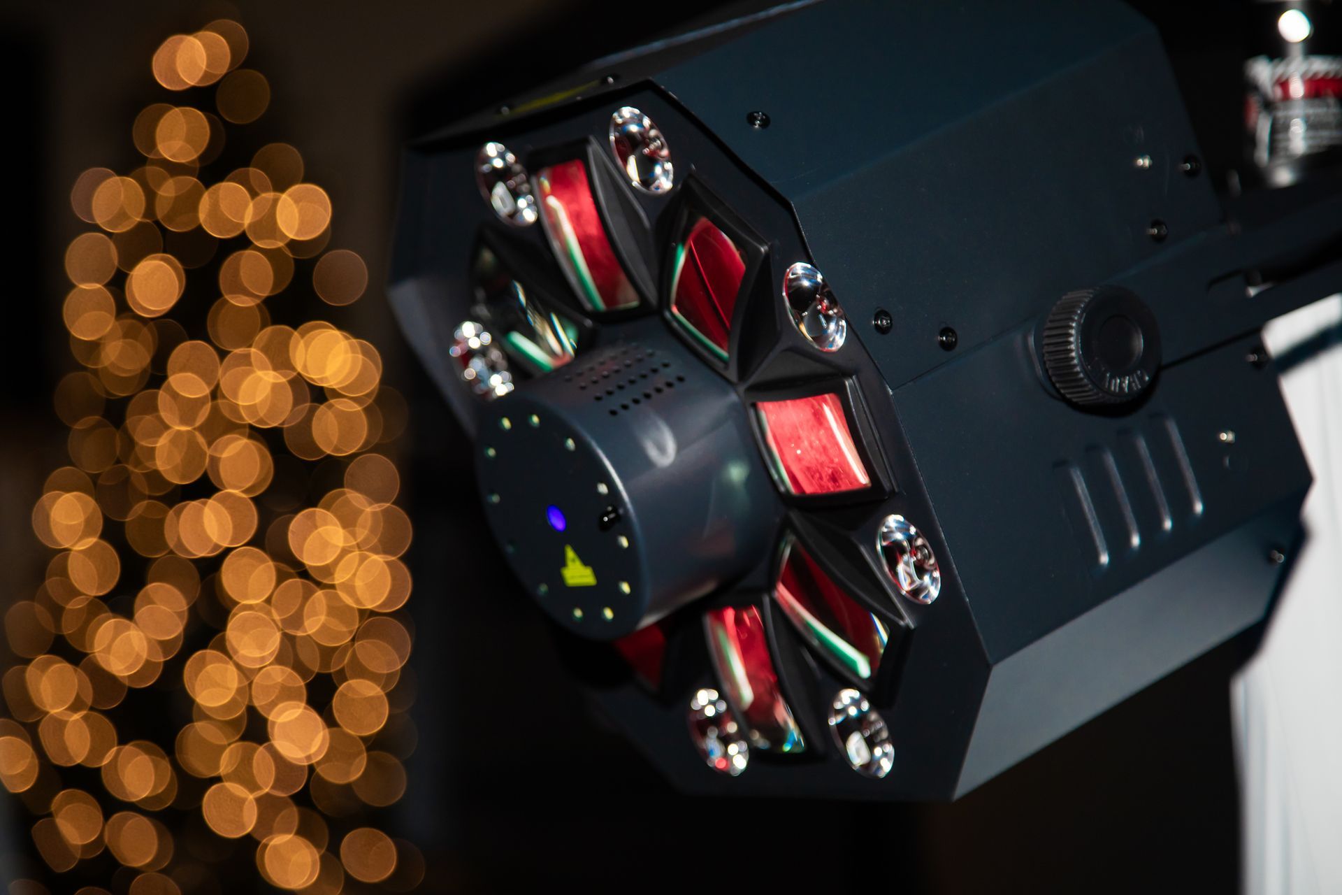Black stage light with red and green elements, in front of blurred golden lights.