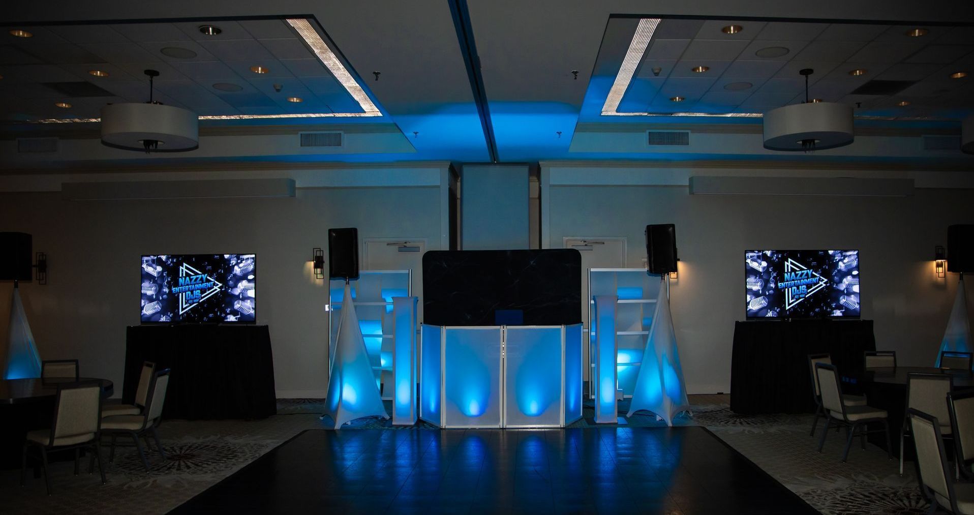 Event stage with blue lighting, screens, and speakers in a ballroom.