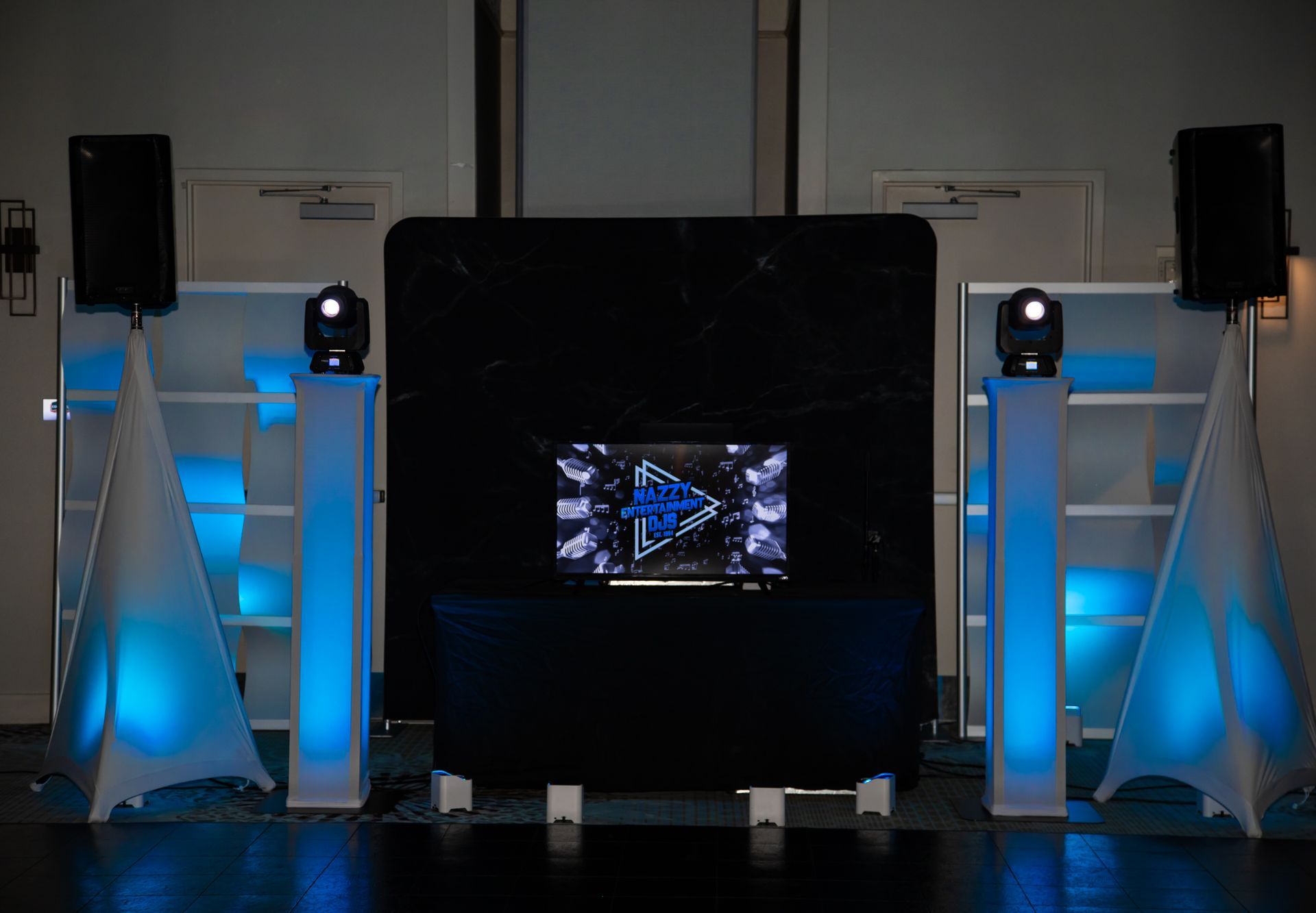 DJ setup with speakers, lights, and a screen, illuminated with blue lights.
