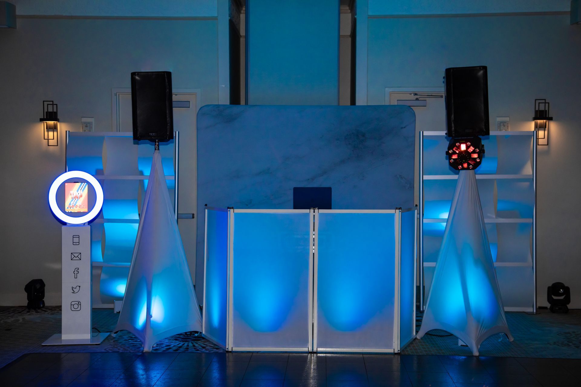 DJ setup with blue lighting, speakers, a photo booth, and geometric shapes.
