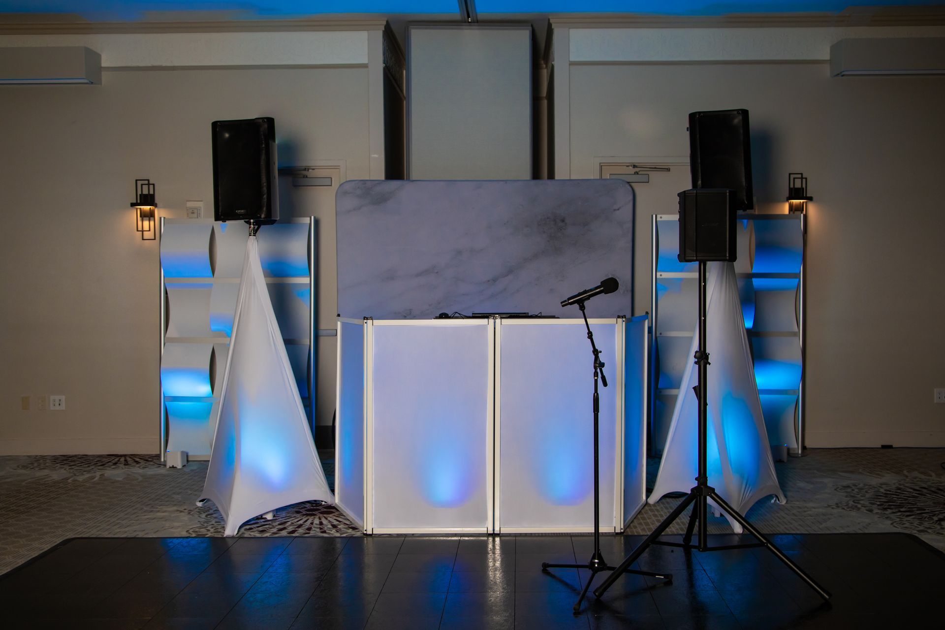 DJ setup on stage, with speakers, microphone, and illuminated panels in a venue.