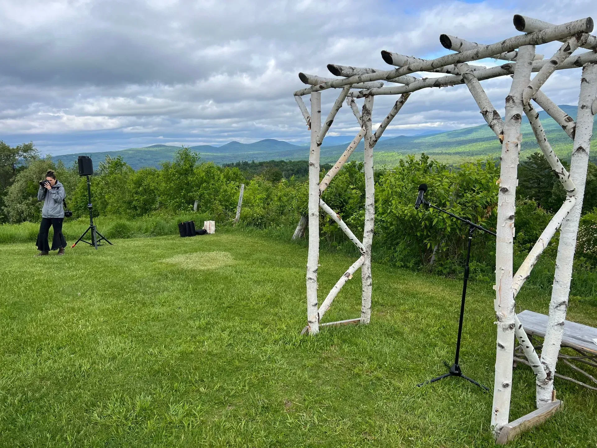 Wedding arch overlooking mountains, photographer with camera, grassy setting.