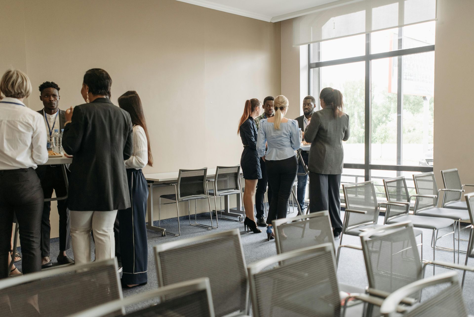 People networking in a room with rows of chairs near a large window.