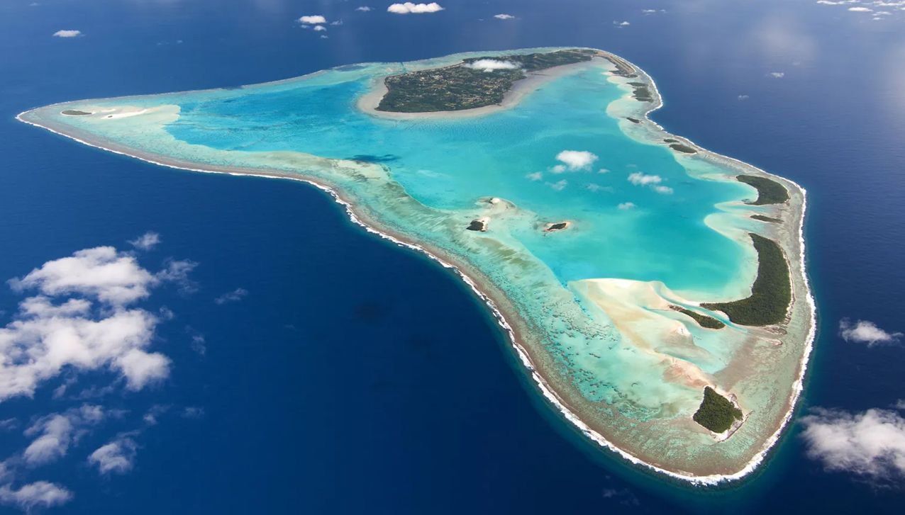 An aerial view of a tropical coral atoll surrounded by vibrant turquoise lagoons and deep blue ocean waters.