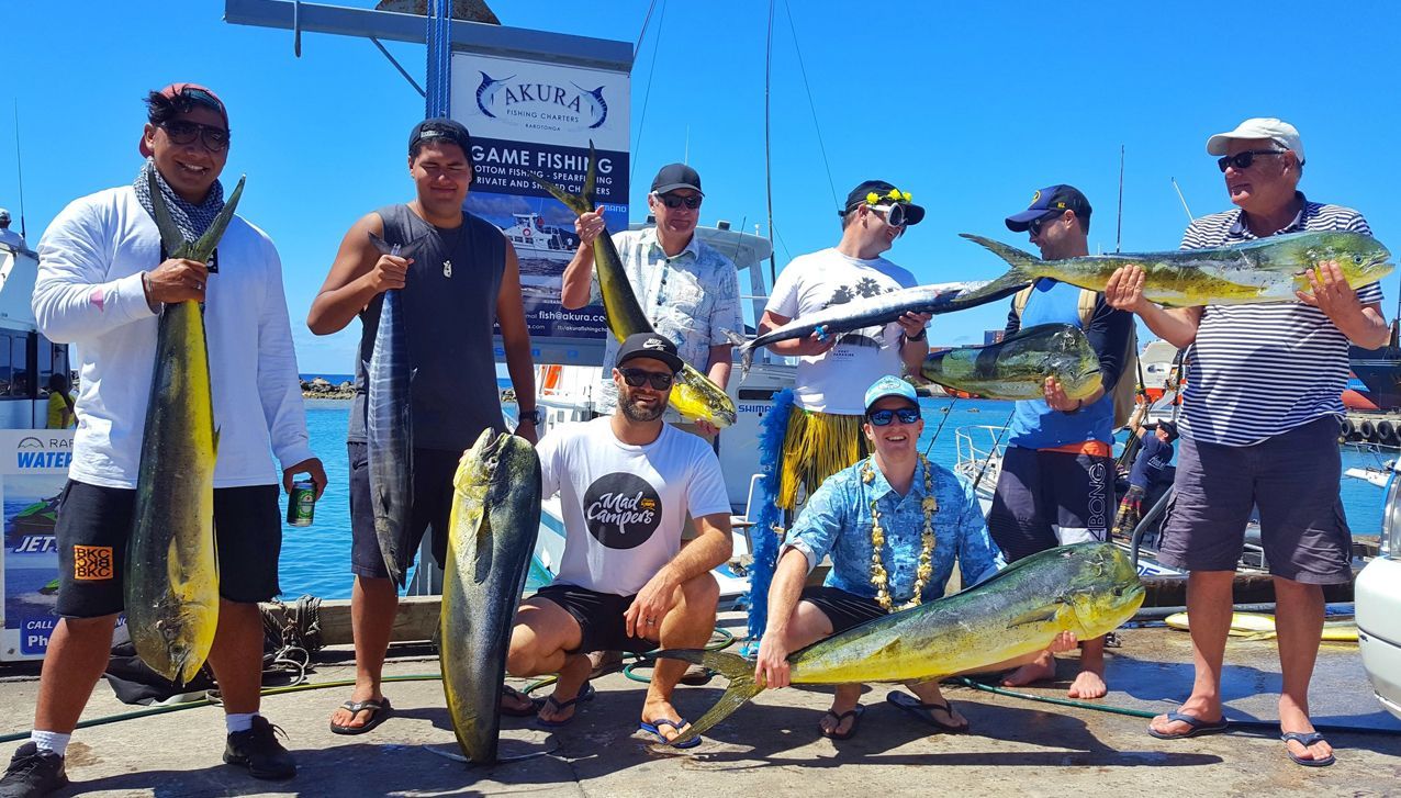A group of people standing on a dock holding large, freshly caught mahi-mahi fish under a clear blue sky.