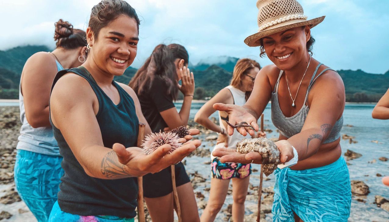People standing on a rocky beach holding various marine life in their hands, looking toward the camera.