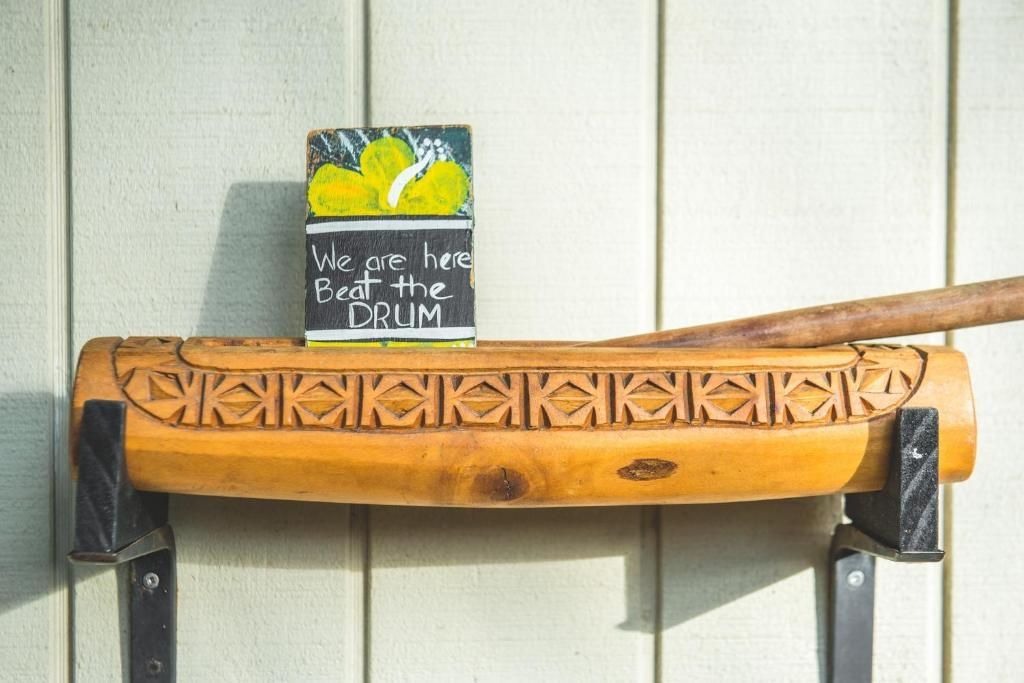A wooden carved drum rests on black wall mounts with a small sign featuring yellow lemons and text on top.