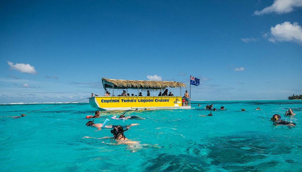 People snorkeling in bright blue water near a yellow tour boat with a thatched roof under a clear sunny sky.