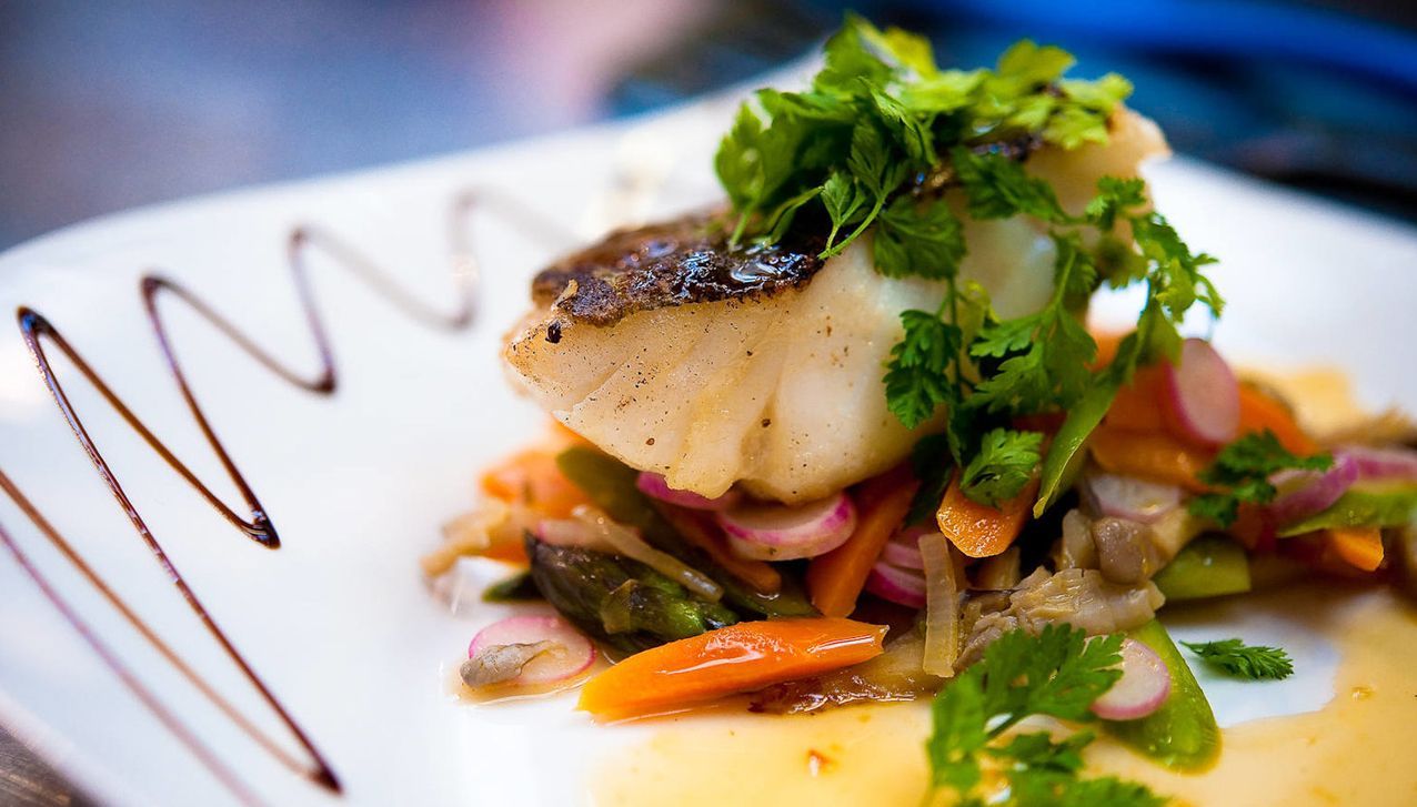 A pan-seared white fish fillet topped with fresh cilantro, served over a bed of sautéed vegetables with a balsamic drizzle.