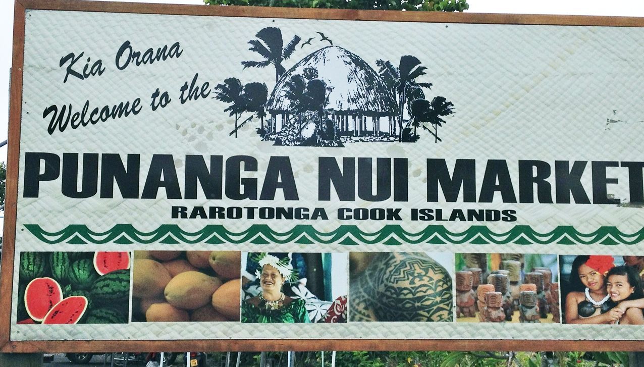A large, rectangular sign for the Punanga Nui Market in Rarotonga, Cook Islands, featuring an image of a traditional hut.