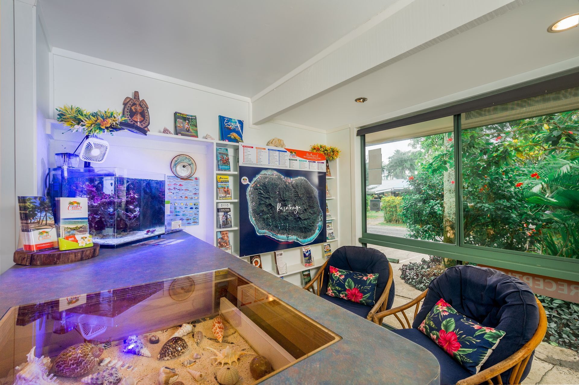 Indoor room featuring a large illuminated aquarium, a coral display on a screen, and two patterned chairs by a window.