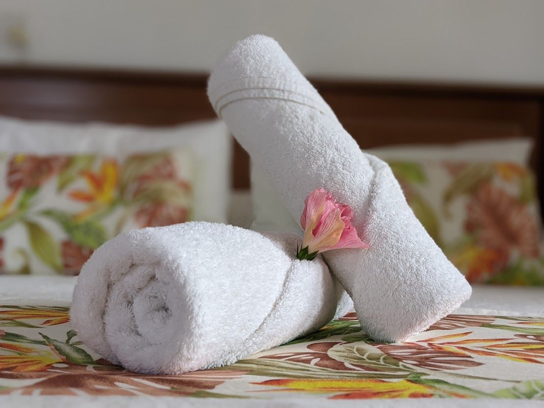 Two rolled white towels with a small pink flower sitting on a tropical-patterned bedspread.