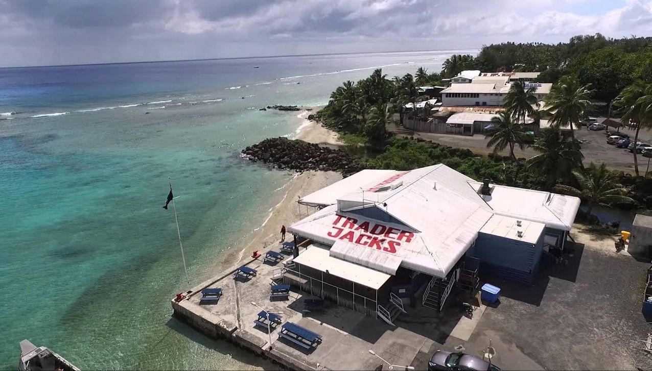 Aerial view of Trader Jack's restaurant on a coastal pier surrounded by blue ocean water and tropical vegetation.