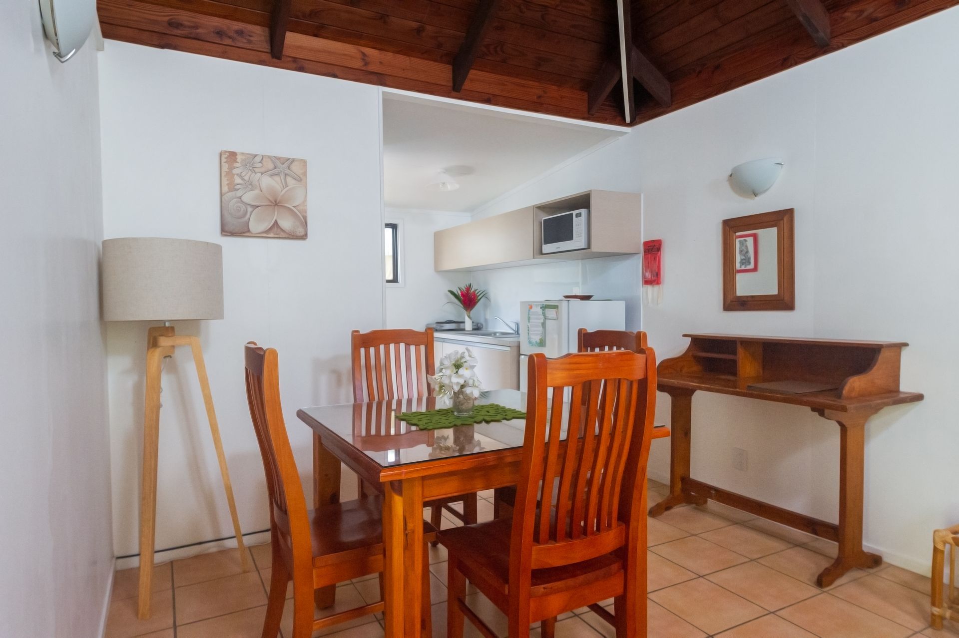 Dining area with a wooden table, four chairs, a floor lamp, and a hallway leading to a kitchen with cabinets.