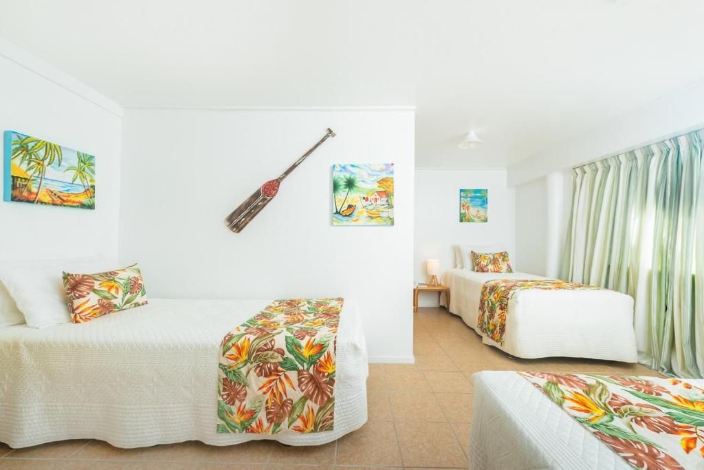A hotel room with two twin beds featuring tropical-print runners, white walls, wall art, and an oar, plus a third bed.