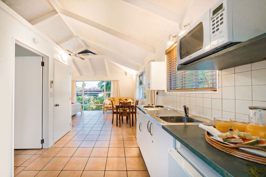 A modern kitchenette with white cabinets and a microwave opens into a sunlit dining area with tile flooring.