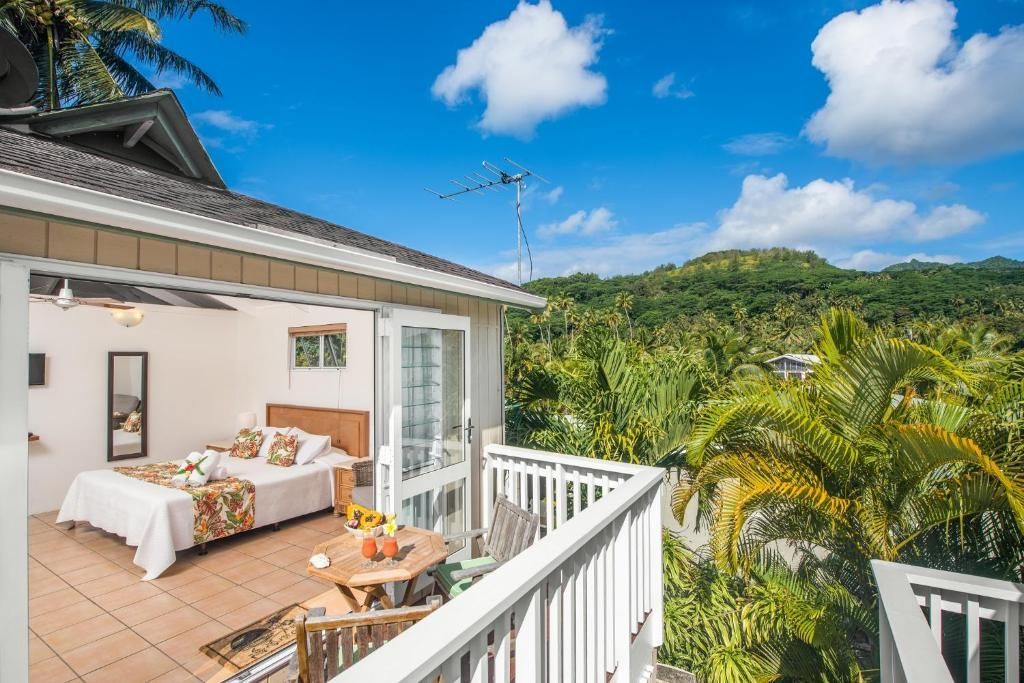 A bedroom opens onto a white-railed balcony overlooking a lush tropical landscape under a bright, sunny sky.