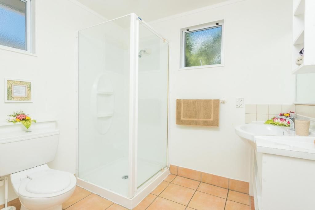 A bright bathroom featuring a white toilet, a walk-in shower with glass doors, a sink, and tan tile flooring.