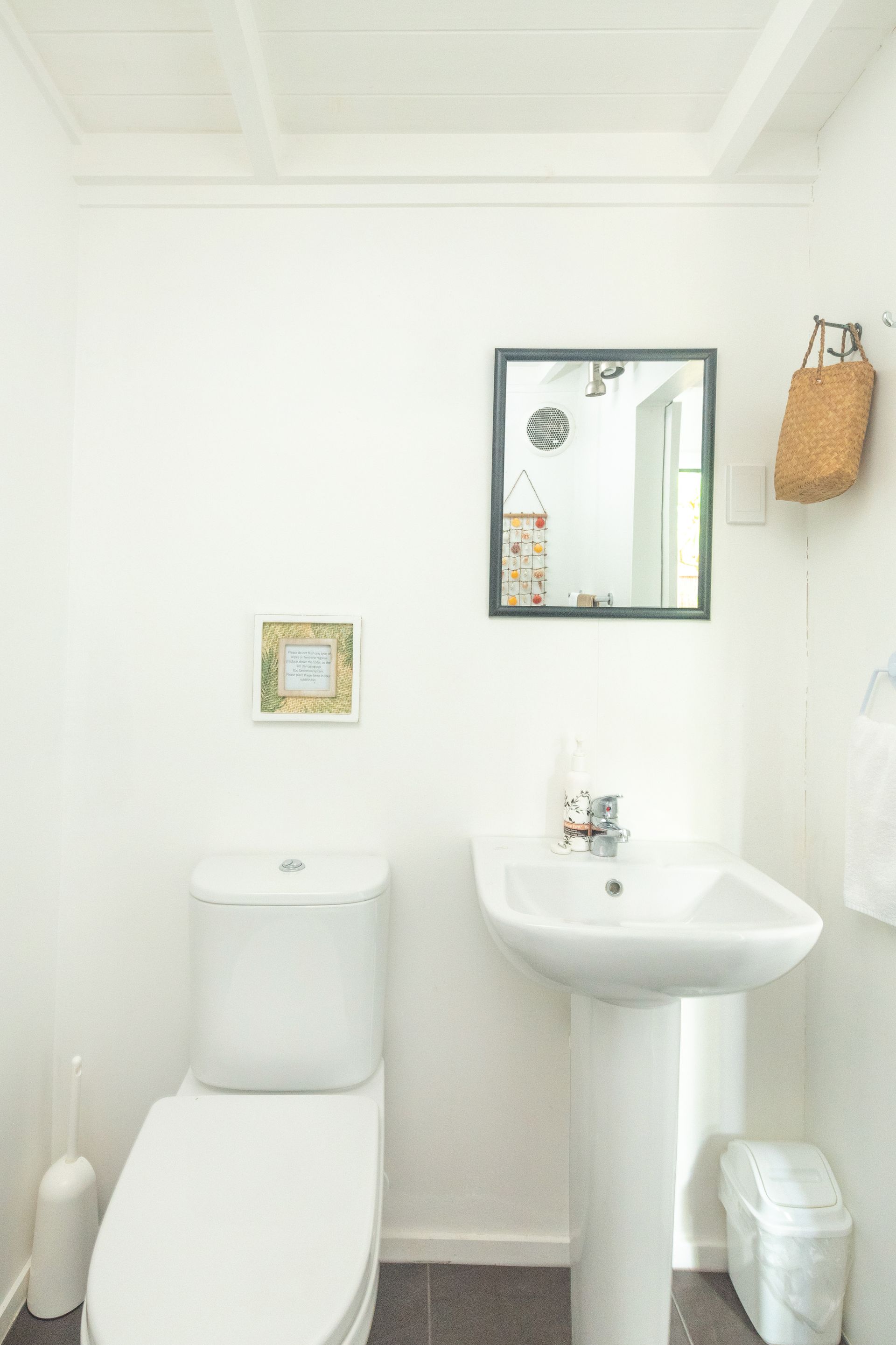 A white pedestal sink and a toilet in a small, minimalist bathroom with white walls and a small wall mirror.