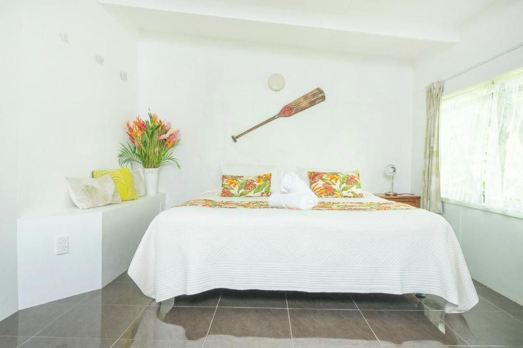 A bright bedroom with a white bed, floral pillows, and a wooden oar mounted on the wall above.