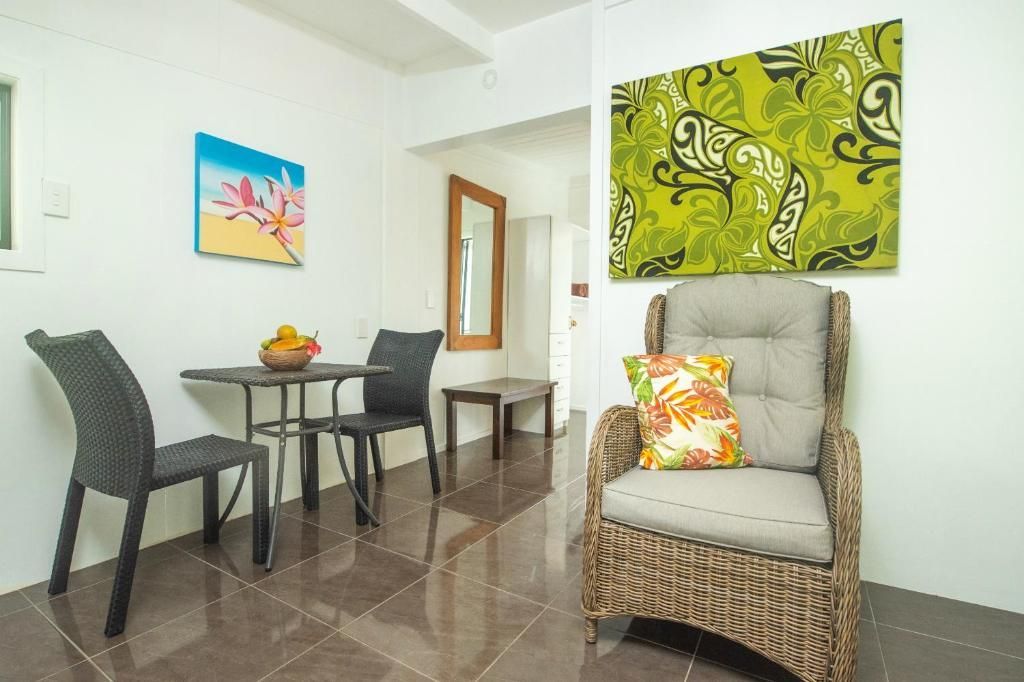 A wicker armchair and a small dining set with two chairs in a bright, modern room with tiled floors and wall art.