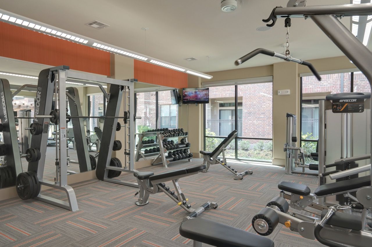 Indoor community gym with weight racks, benches, and cardio machines.