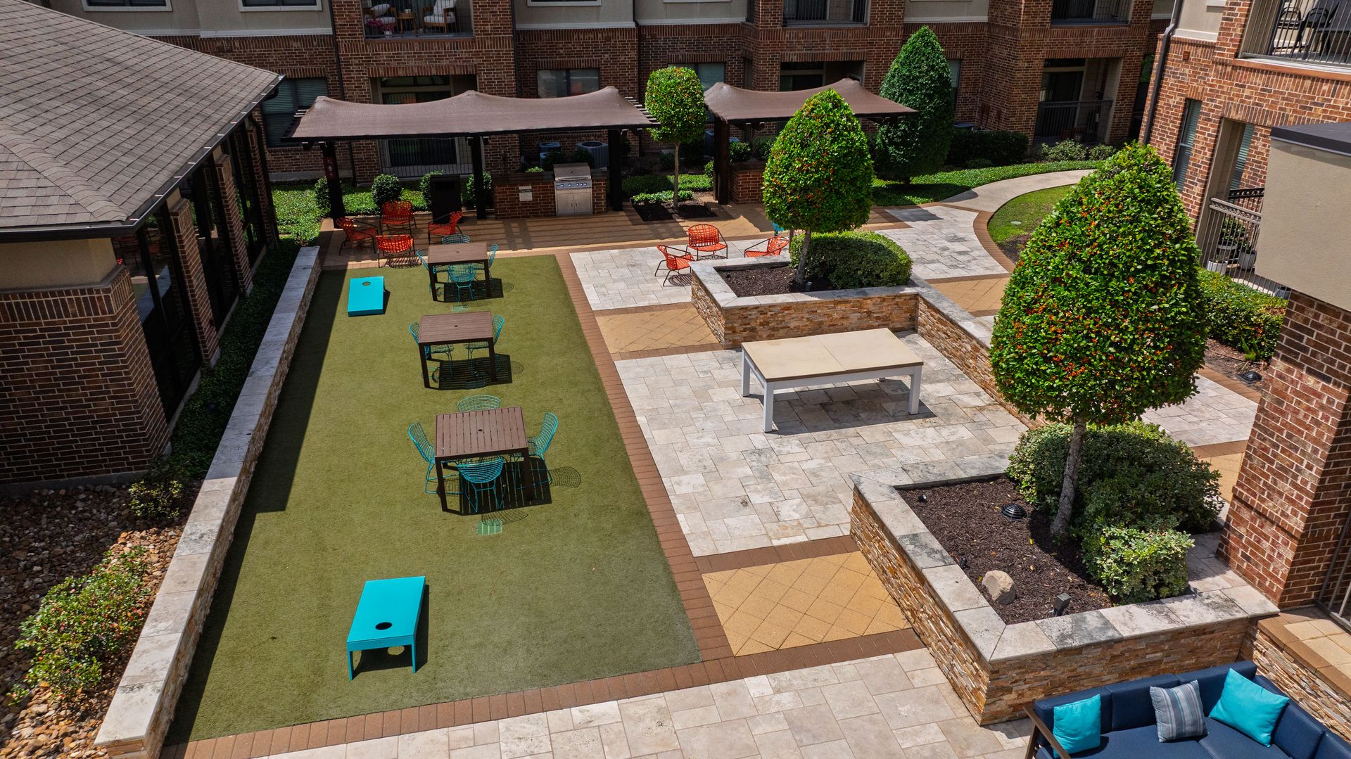 Courtyard patio with green turf, lounge chairs, planters, and brick buildings around a central seating area at Olympus Sierra Pines at The Woodlands, TX