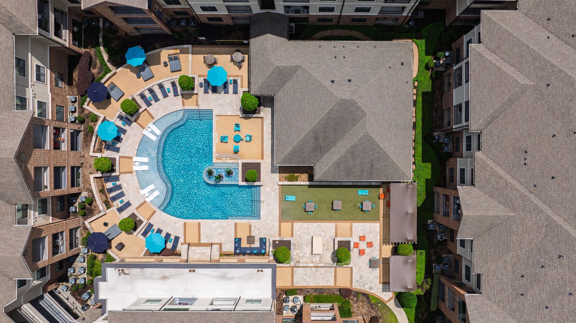 Aerial view of a resort pool deck with blue umbrellas, lounge chairs, and surrounding hotel buildings at Olympus Sierra Pines at The Woodlands, TX