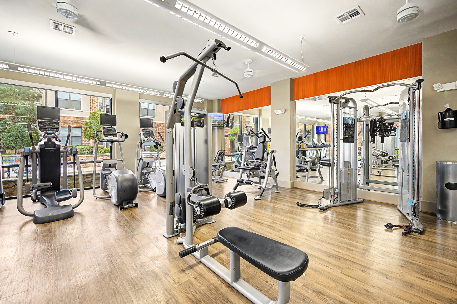 Bright modern gym with exercise machines, mirrors, and wooden flooring at Olympus Sierra Pines at The Woodlands, TX