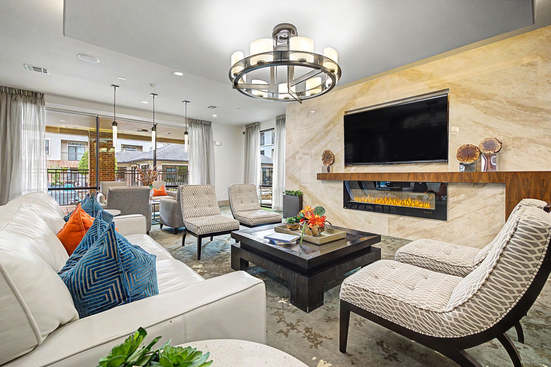 Bright modern living room with white sofas, black coffee table, fireplace, wall-mounted TV, and chandelier at Olympus Sierra Pines at The Woodlands, TX