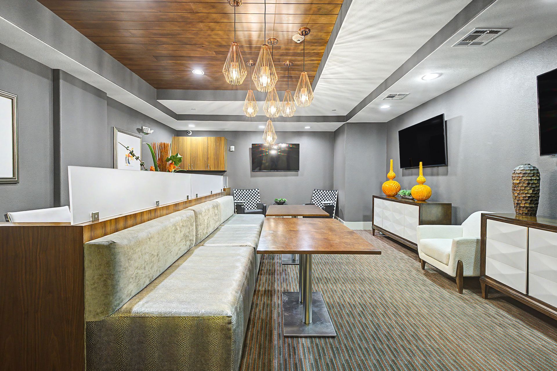 Modern hotel lobby with beige seating, wood tables, chandeliers, and gray walls at Olympus Sierra Pines at The Woodlands, TX