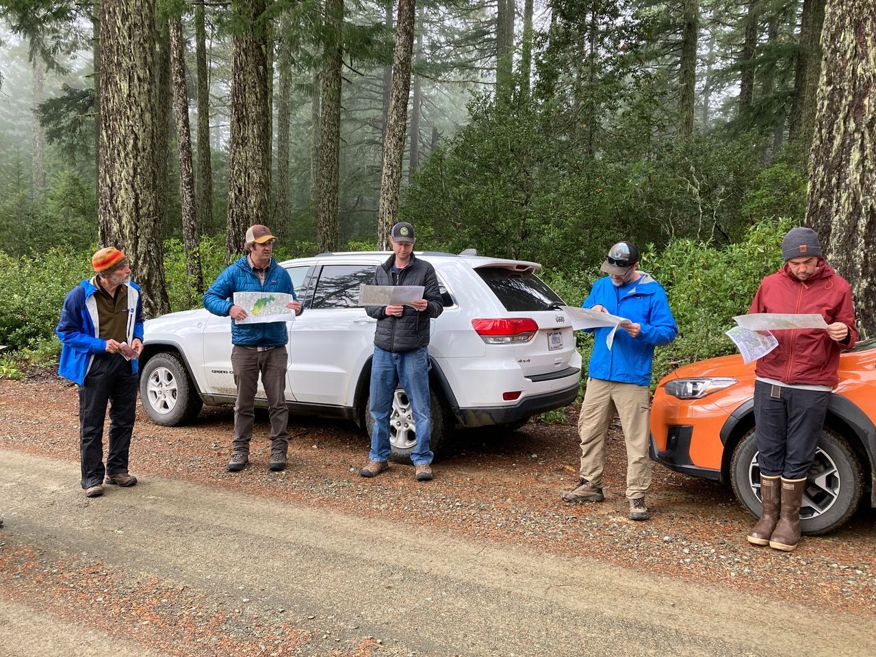 A group of people are standing in front of a car in the woods.