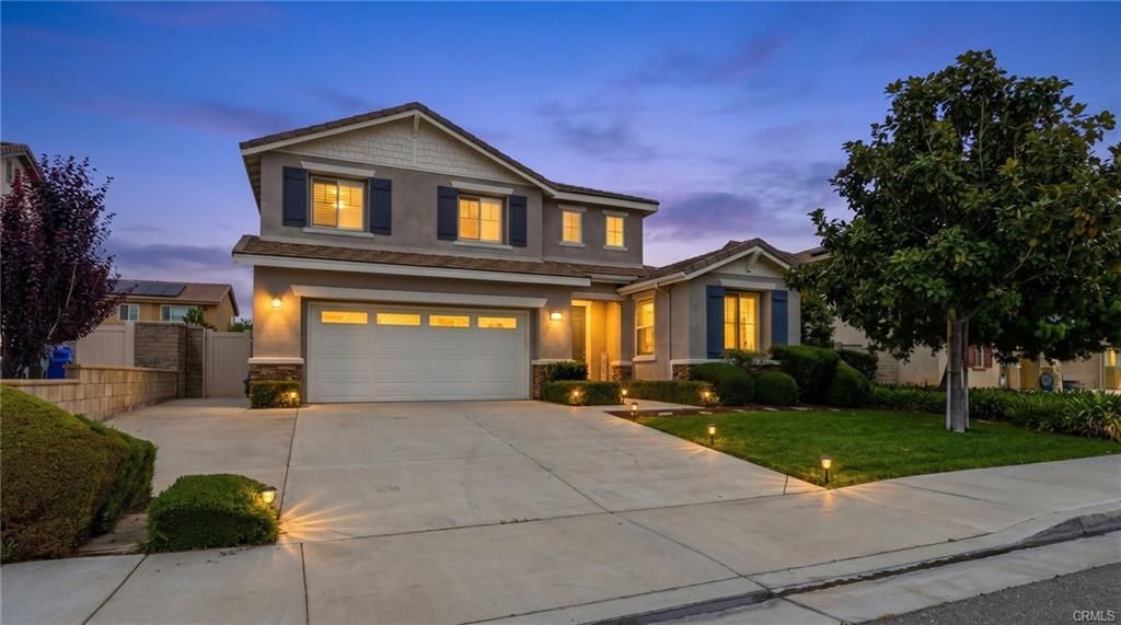 Suburban two-story house at dusk with lit windows, a three-car garage, and a manicured front lawn.