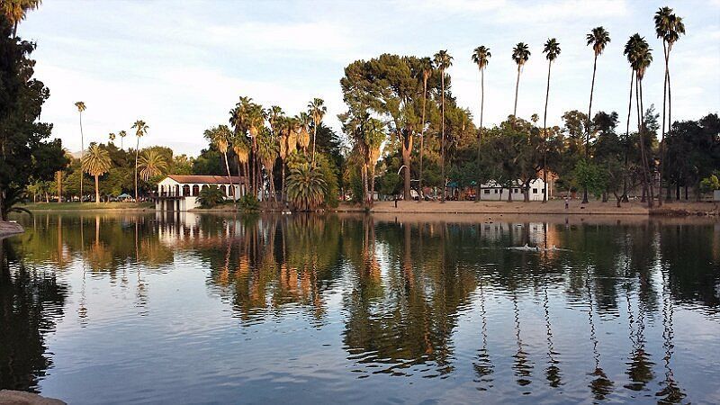 A calm park lake reflecting palm trees and a bridge at sunset