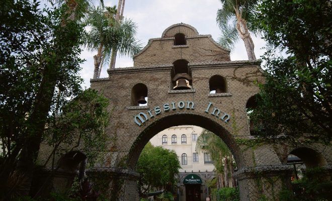 Mansion-style brick archway with arched openings, trees, and a building visible beyond the gate.