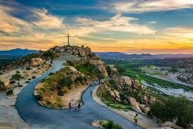 Sunset view of a hilltop cross and winding road above a rocky landscape and valley
