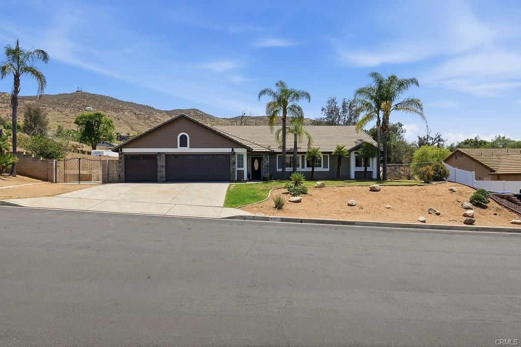 Single-story suburban house with palm trees, a driveway, and desert landscaping under a clear sky
