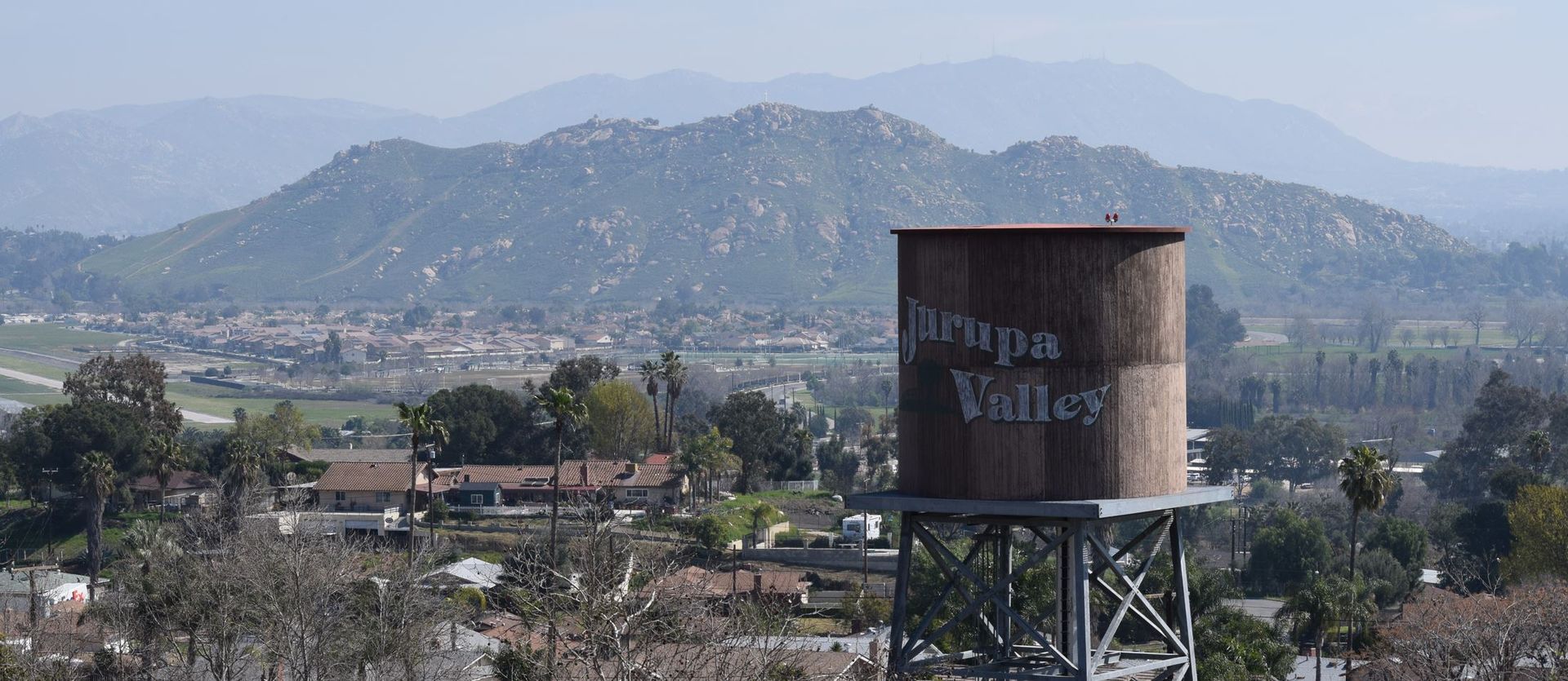 Cylindrical water tank on stilts overlooking a town with mountains in the background.