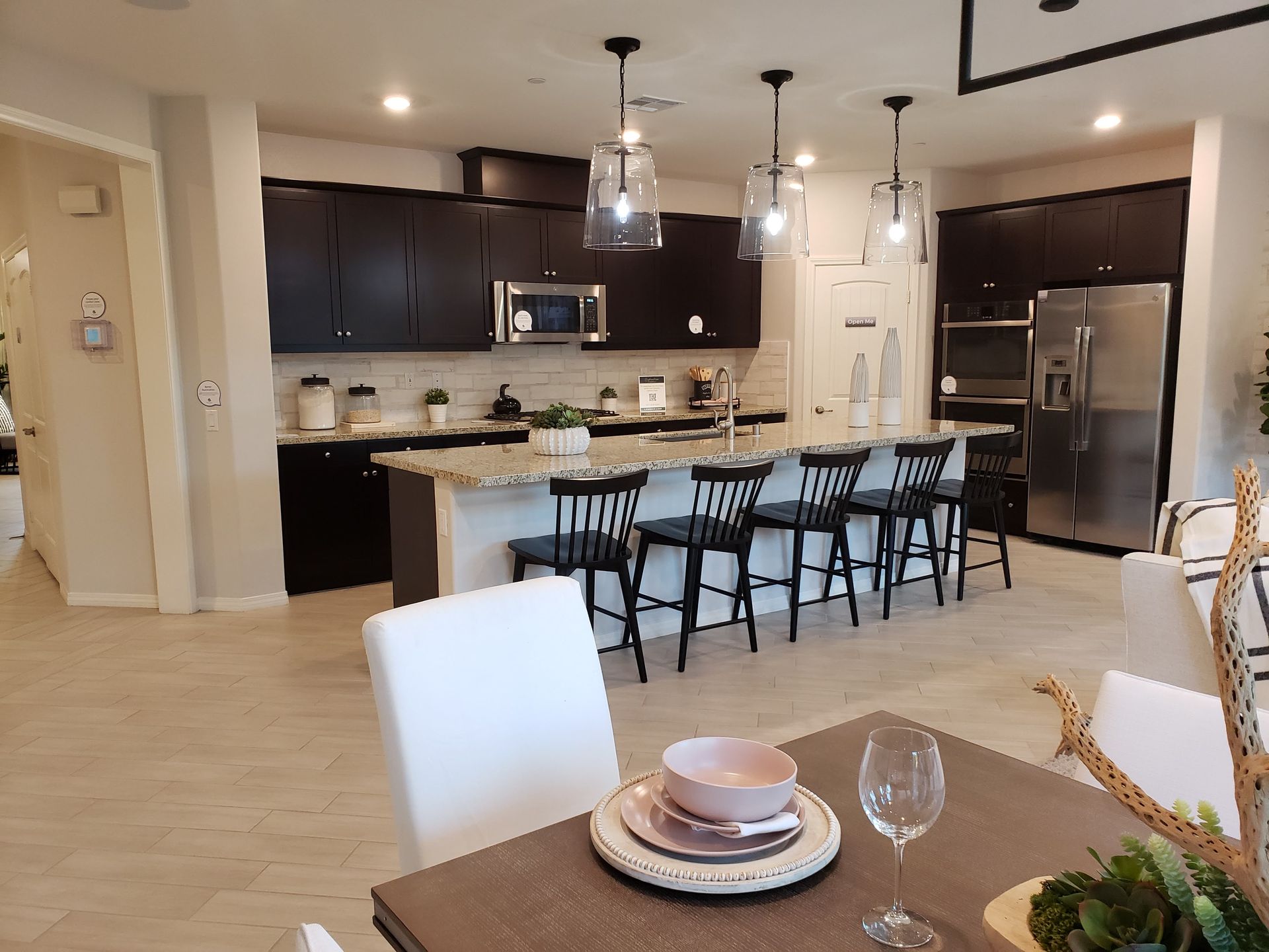 Open kitchen and dining area with dark cabinets, pendant lights, and a set dining table in the foreground