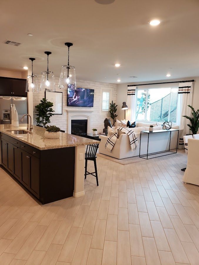 Bright open-concept kitchen and living room with light wood floors, island, fireplace, and large windows.