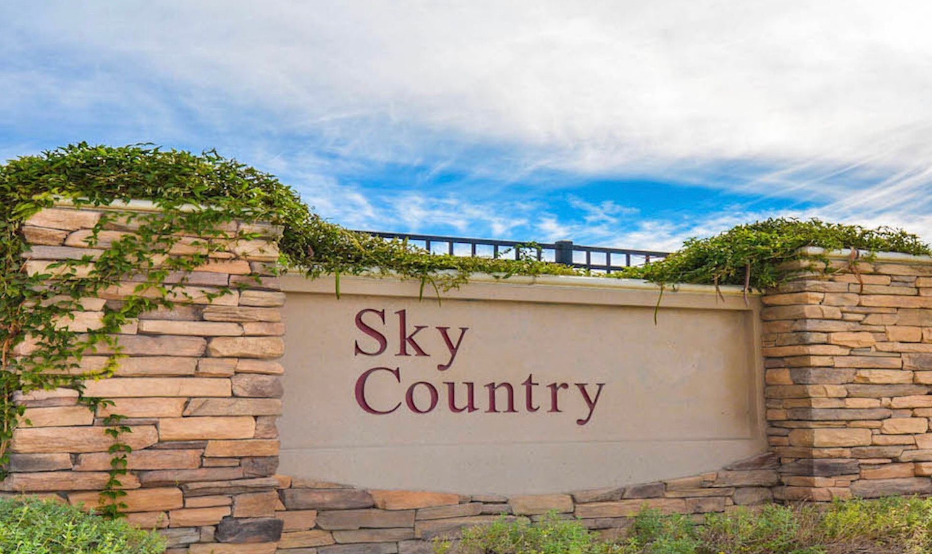 Stone entrance sign reading “Sky Country” against a blue sky with clouds and greenery.