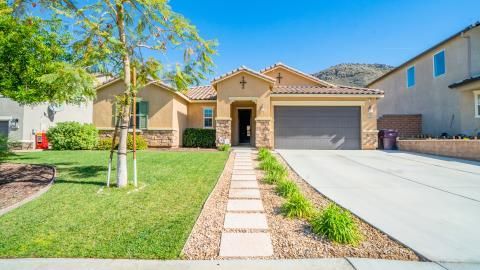 Suburban house with a two-car garage, front lawn, stone walkway, and driveway under bright sunlight
